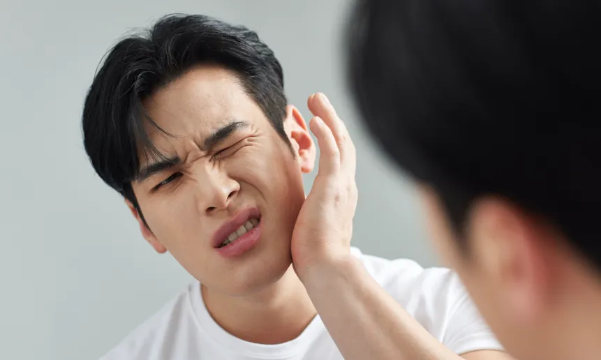 거울을 보며 턱을 잡고 고통스러워하는 남성