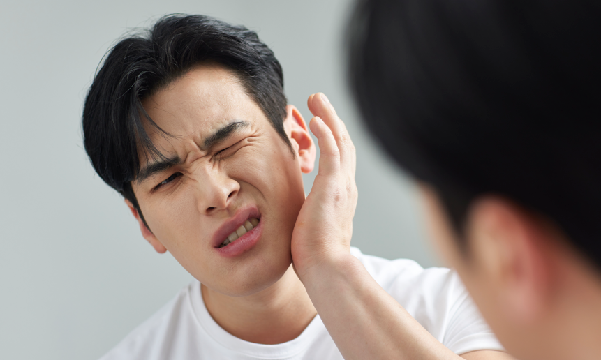 거울을 보며 턱을 잡고 고통스러워하는 남성