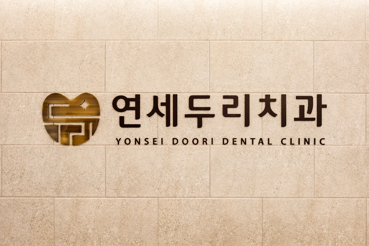 베이지색 타일 벽에 '연세두리치과 YONSEI DOORI DENTAL CLINIC'이라고 적힌 간판이 걸려 있다.