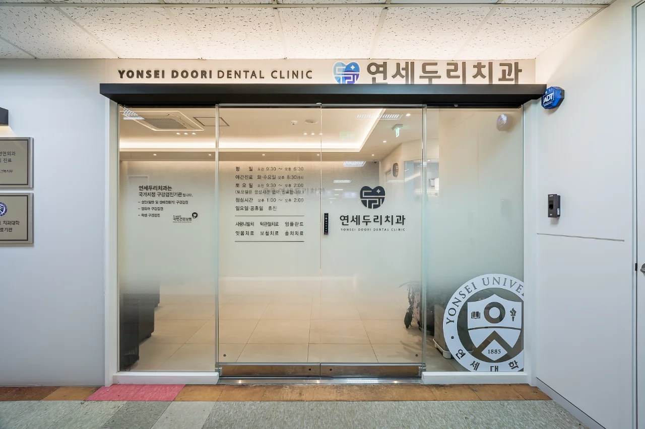 연세두리치과 입구 전경. 유리 자동문과 병원 이름, 진료 시간표가 보인다.
